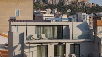 A modern building with a rooftop terrace featuring lounge chairs and a glass balustrade.