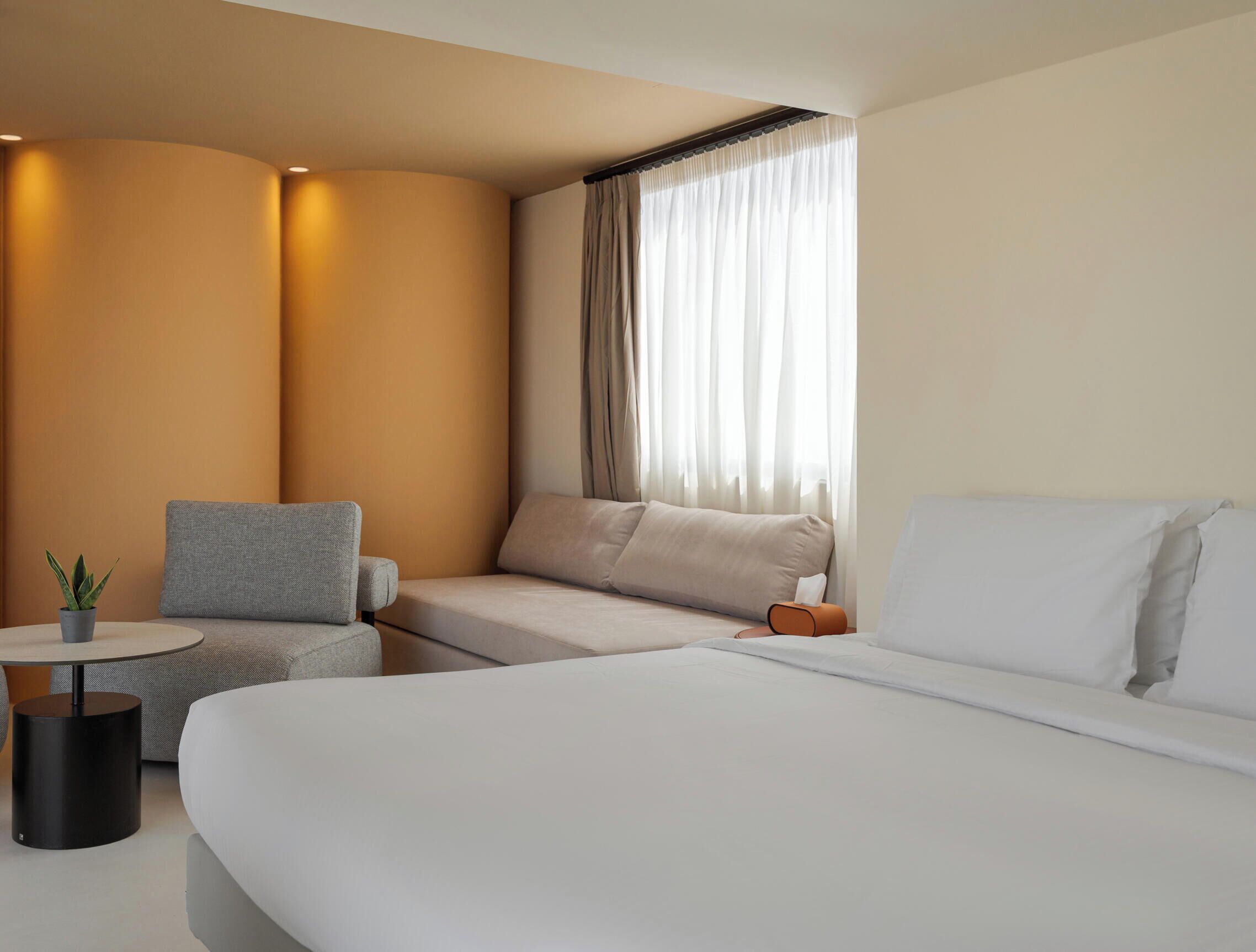 A hotel room with a bed, a seating area with a chair and a small table, and a window with curtains.