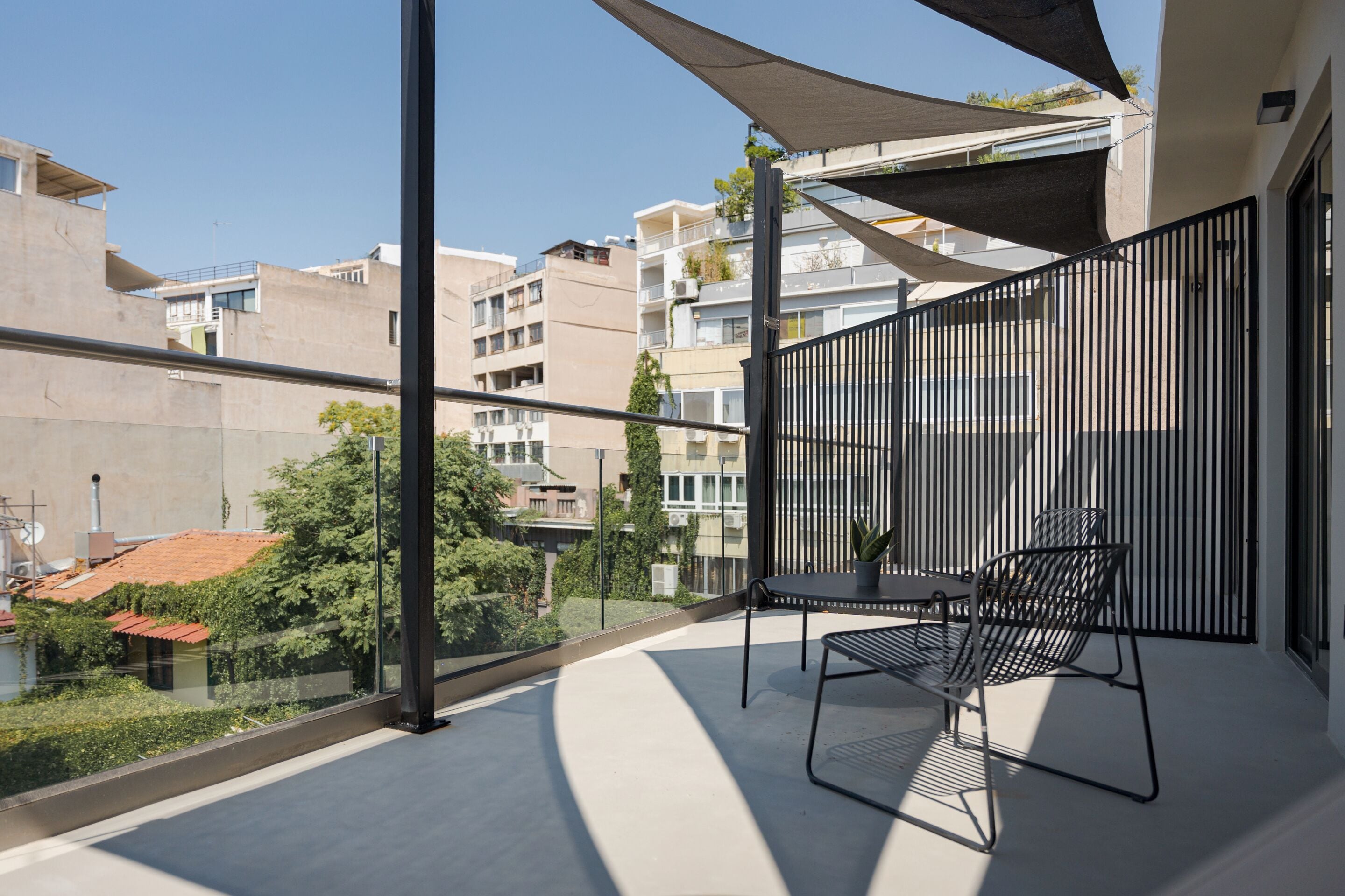 Un balcone con tavolo e sedie, vista sui palazzi vicini e cielo sereno.