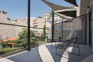 A balcony with a table and chairs, a view of neighboring buildings, and a clear sky.