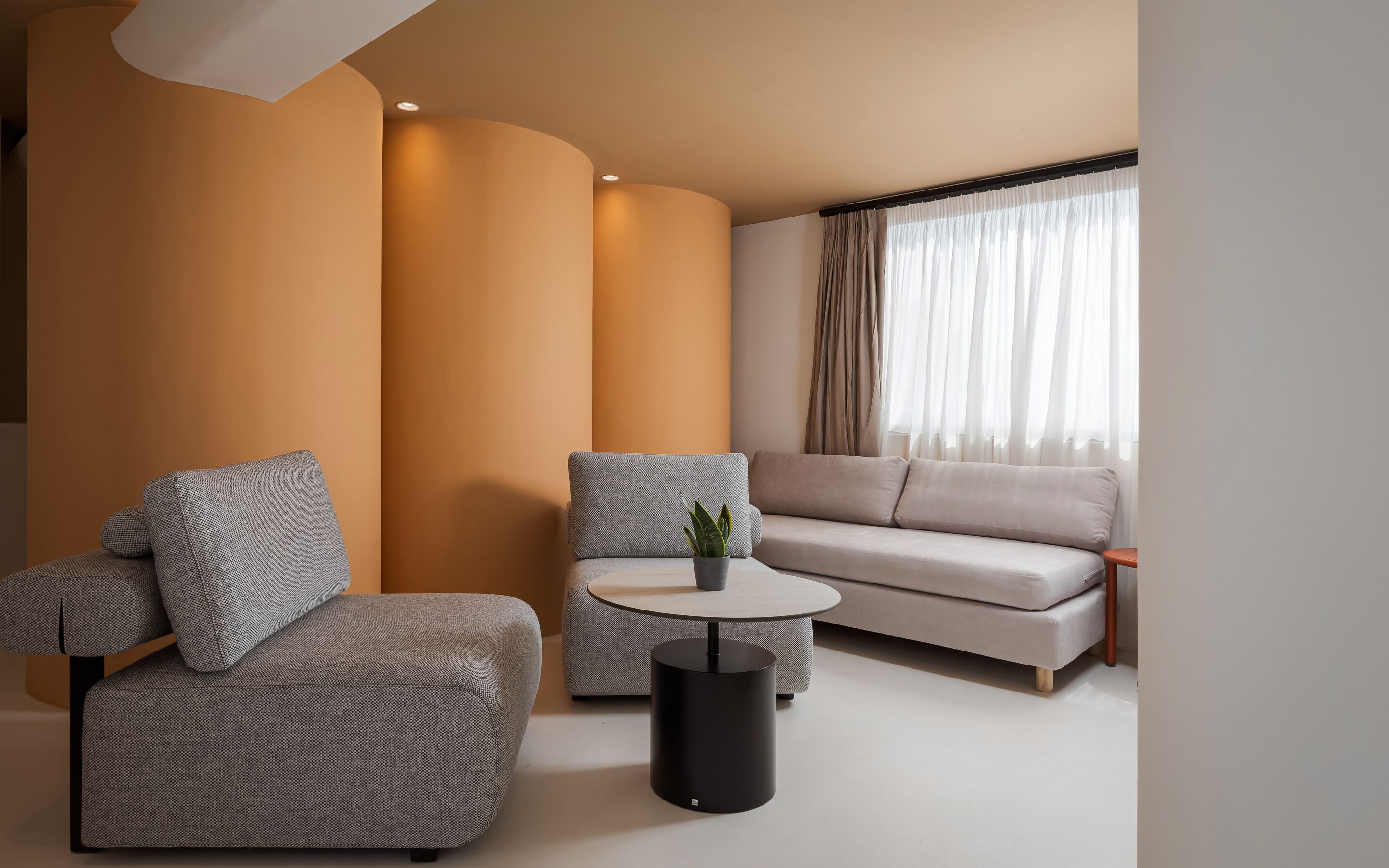 Een moderne woonkamer met een bank, twee fauteuils, een salontafel en een plant in pot.