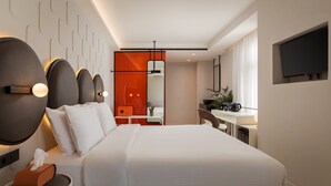 A modern hotel room with a large bed, bedside tables, a flat-screen TV, and a bathroom with a mirror and sink.