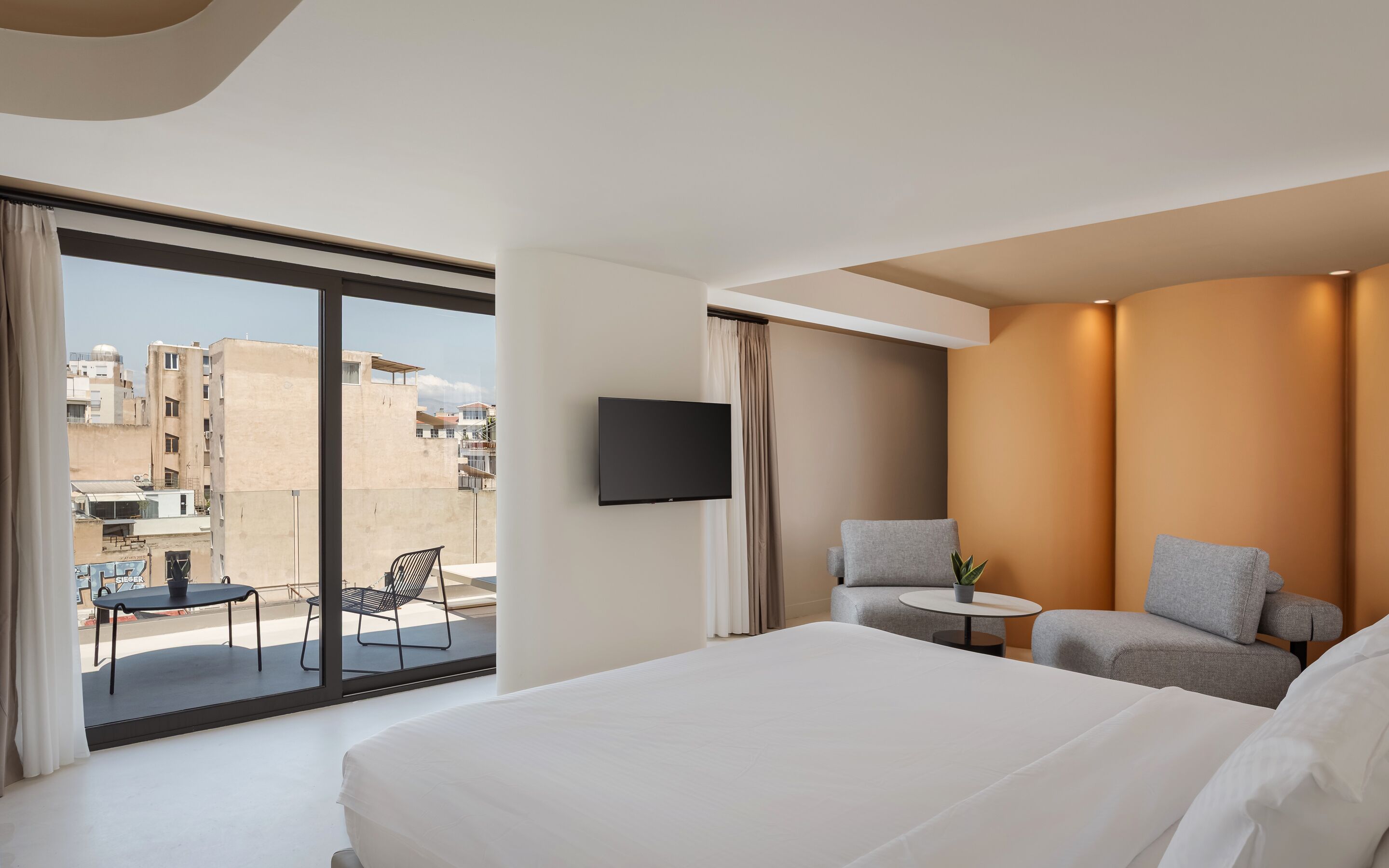 Habitación de hotel con una cama grande, un televisor montado en la pared y un balcón con mesa y sillas.