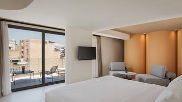 Habitación de hotel con una cama grande, un televisor montado en la pared y un balcón con mesa y sillas.