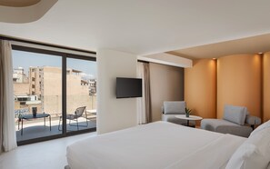 Habitación de hotel con una cama grande, un televisor montado en la pared y un balcón con mesa y sillas.