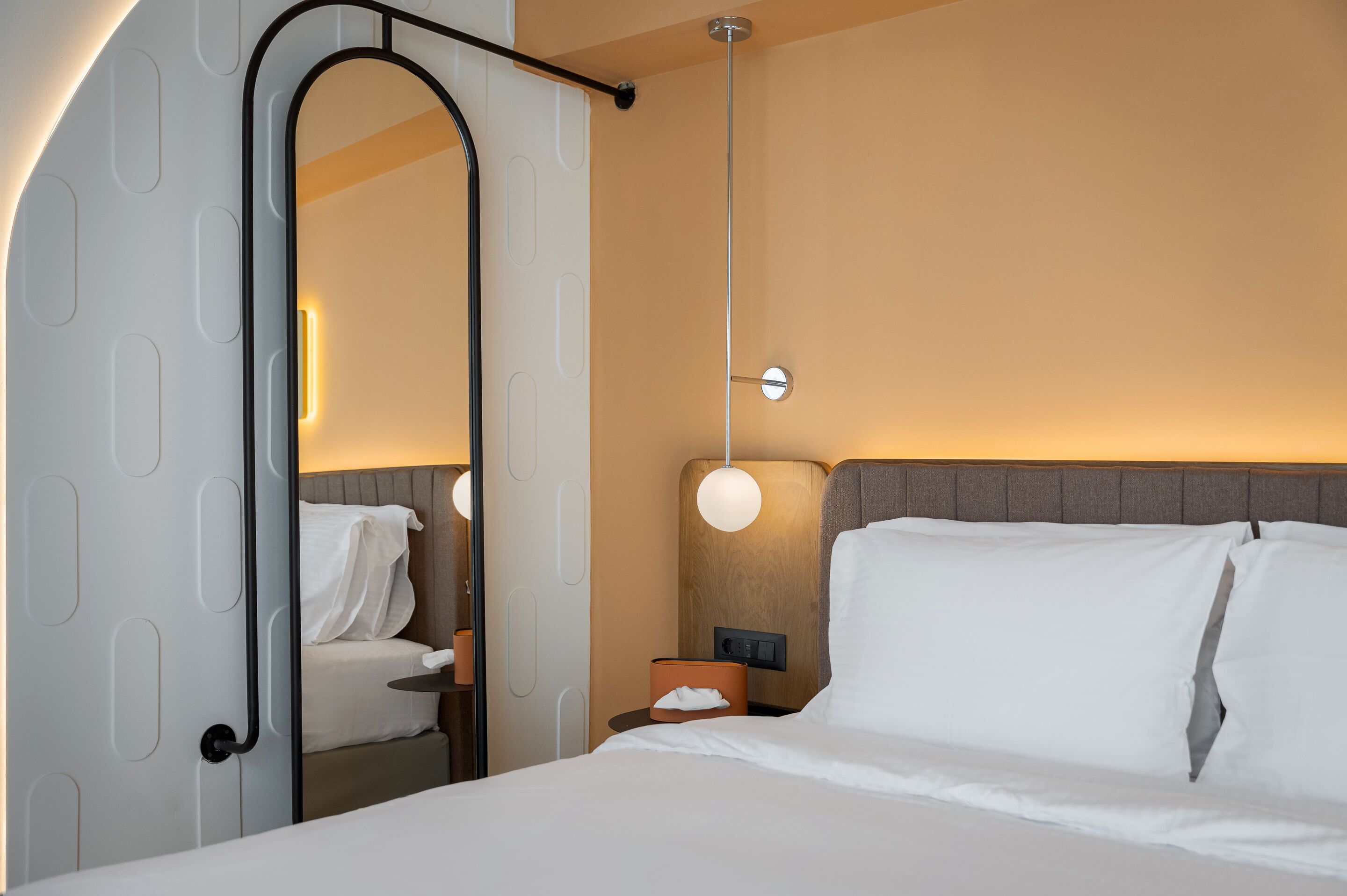 A hotel room with a bed, a nightstand, a lamp, and a mirror.