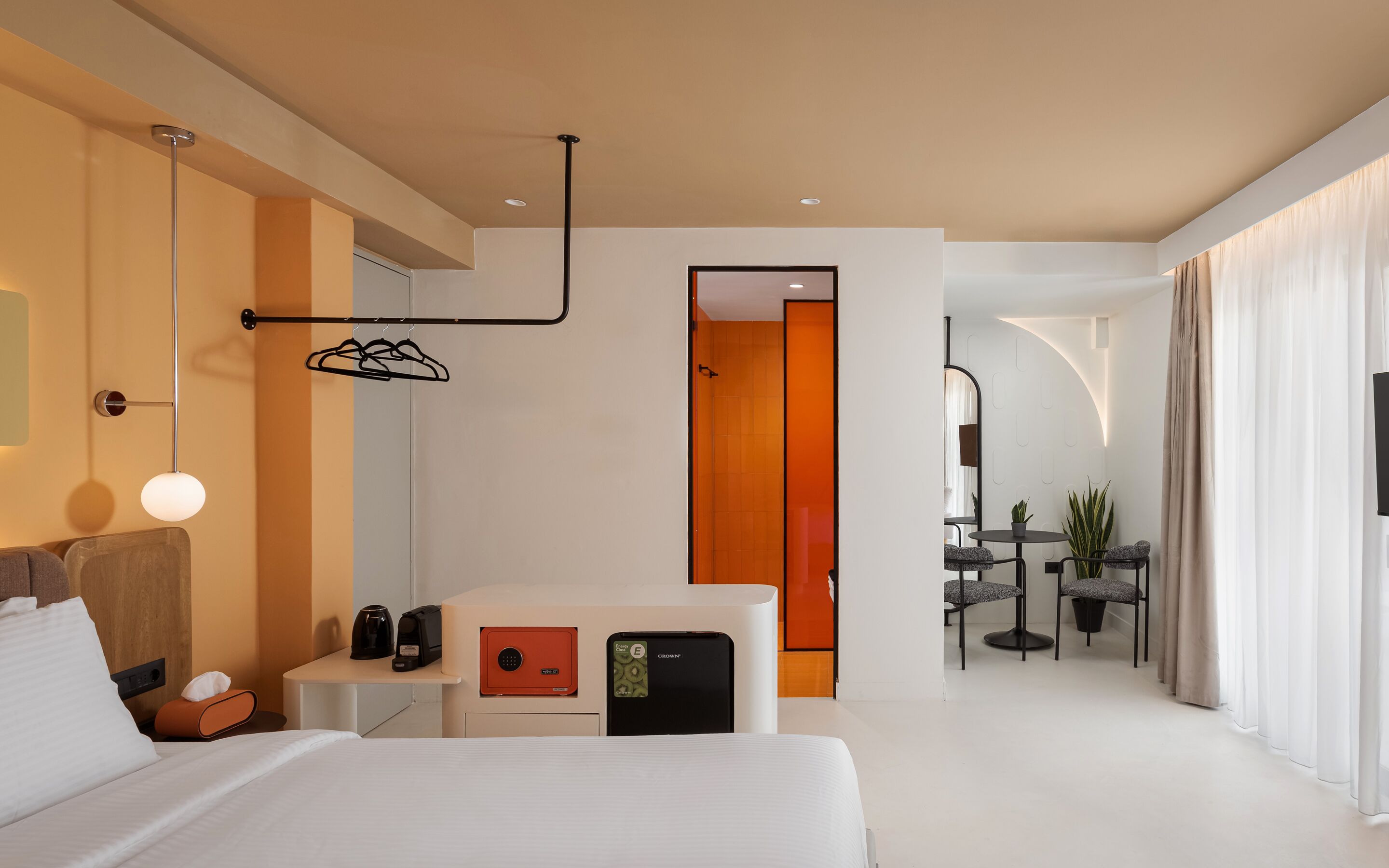 Ein modernes Hotelzimmer mit einem Bett, einem Nachttisch und einem kleinen Schreibtisch mit einem Safe. Ein Badezimmer ist durch eine geöffnete Tür erkennbar.