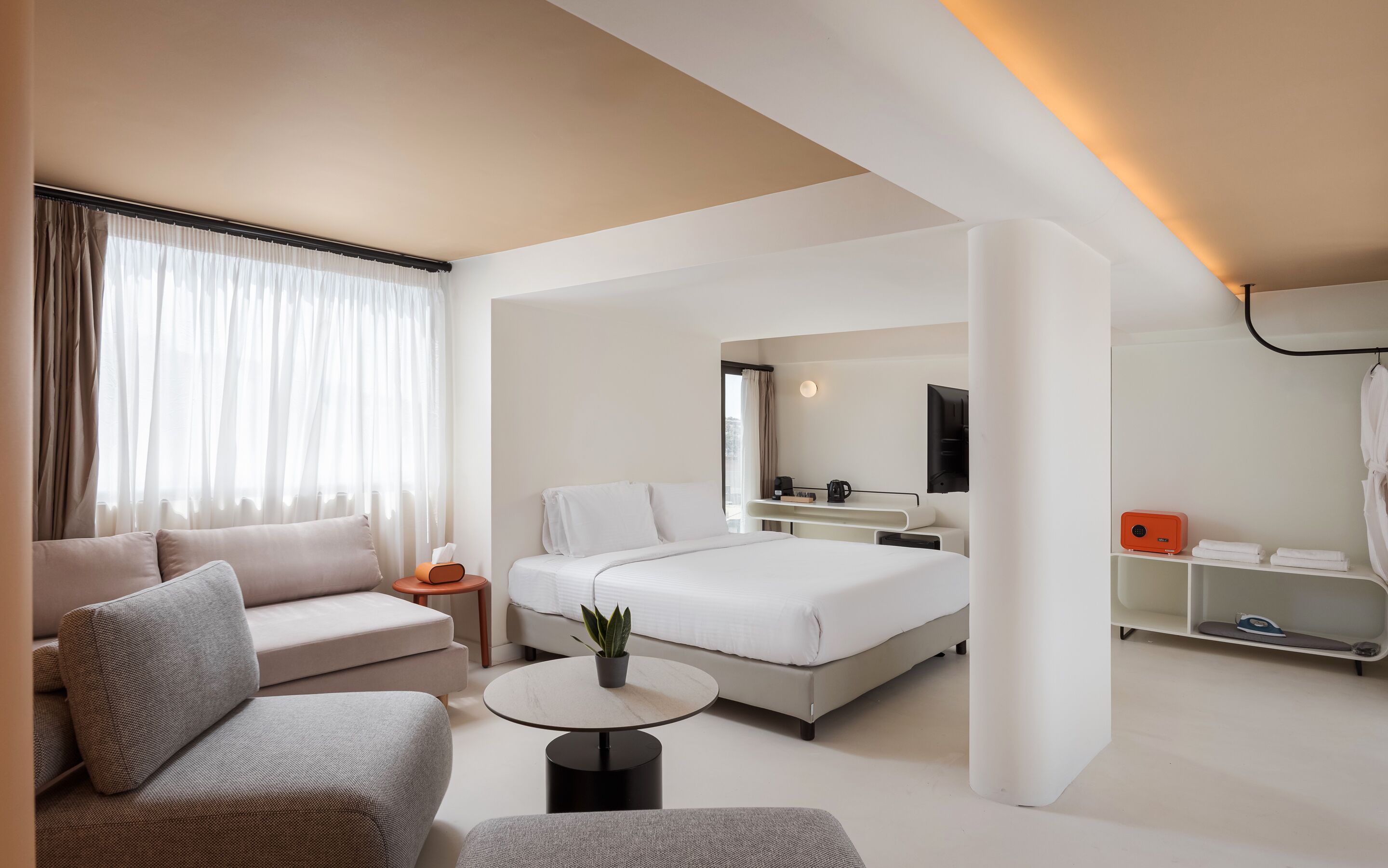 A modern hotel room with a bed, a sofa, a coffee table, and a TV.