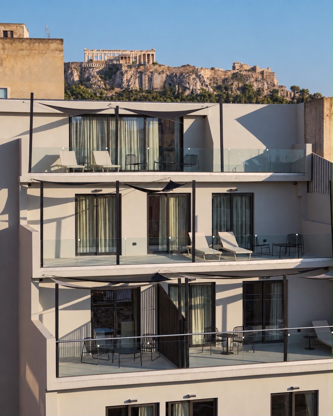A multi-story building with balconies, large windows, and a view of ancient ruins in the background.