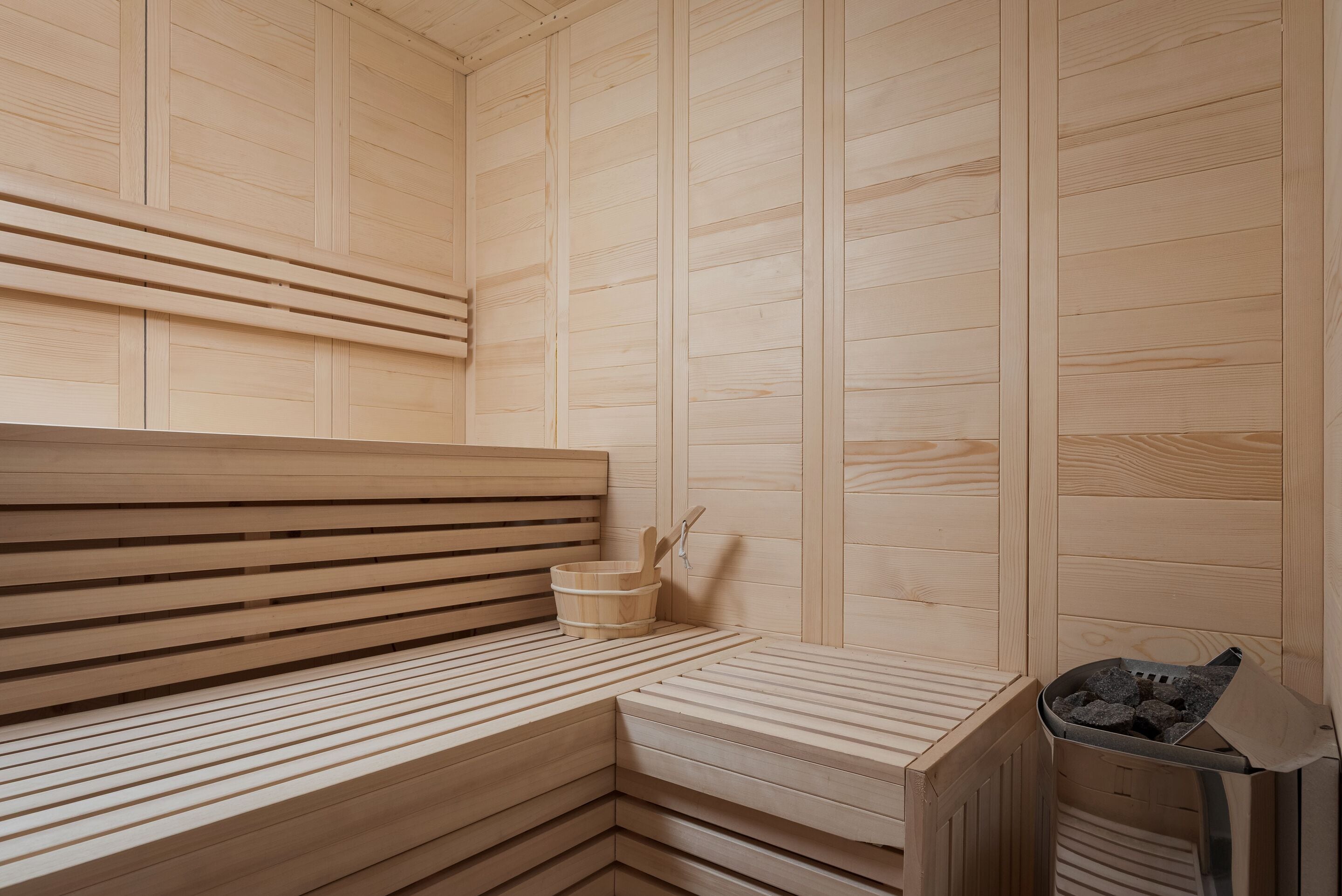 A wooden sauna with benches and a small bucket.
