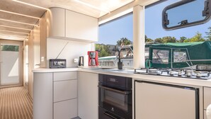 A compact kitchenette with a Bosch coffee maker, a small oven, and a window overlooking a green area.