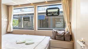 A hotel room with a bed, a window with curtains, a view of the outside, and a small table with a bag on it.