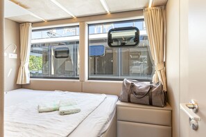 A hotel room with a bed, a window with curtains, a view of the outside, and a small table with a bag on it.