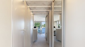 A corridor with a striped floor, leading to a room with a desk and a chair, and a view of the outdoors.