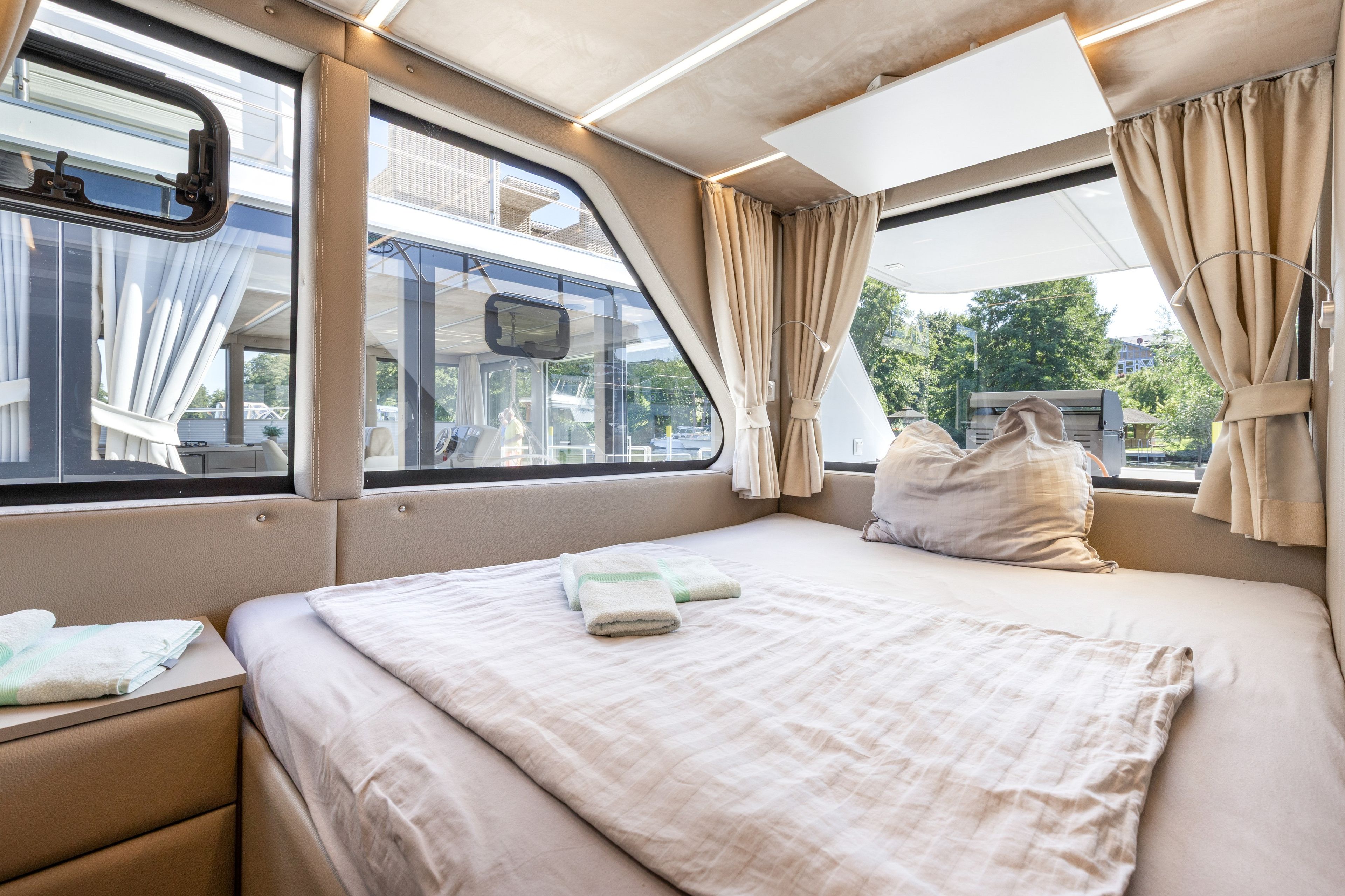 Ein helles, modernes Interieur mit einem Bett, Vorhängen und einem Fenster mit Blick auf ein Gebäude.