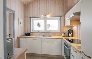 A modern kitchen with wooden panel walls, a window with two flower arrangements, a sink, and a stove.