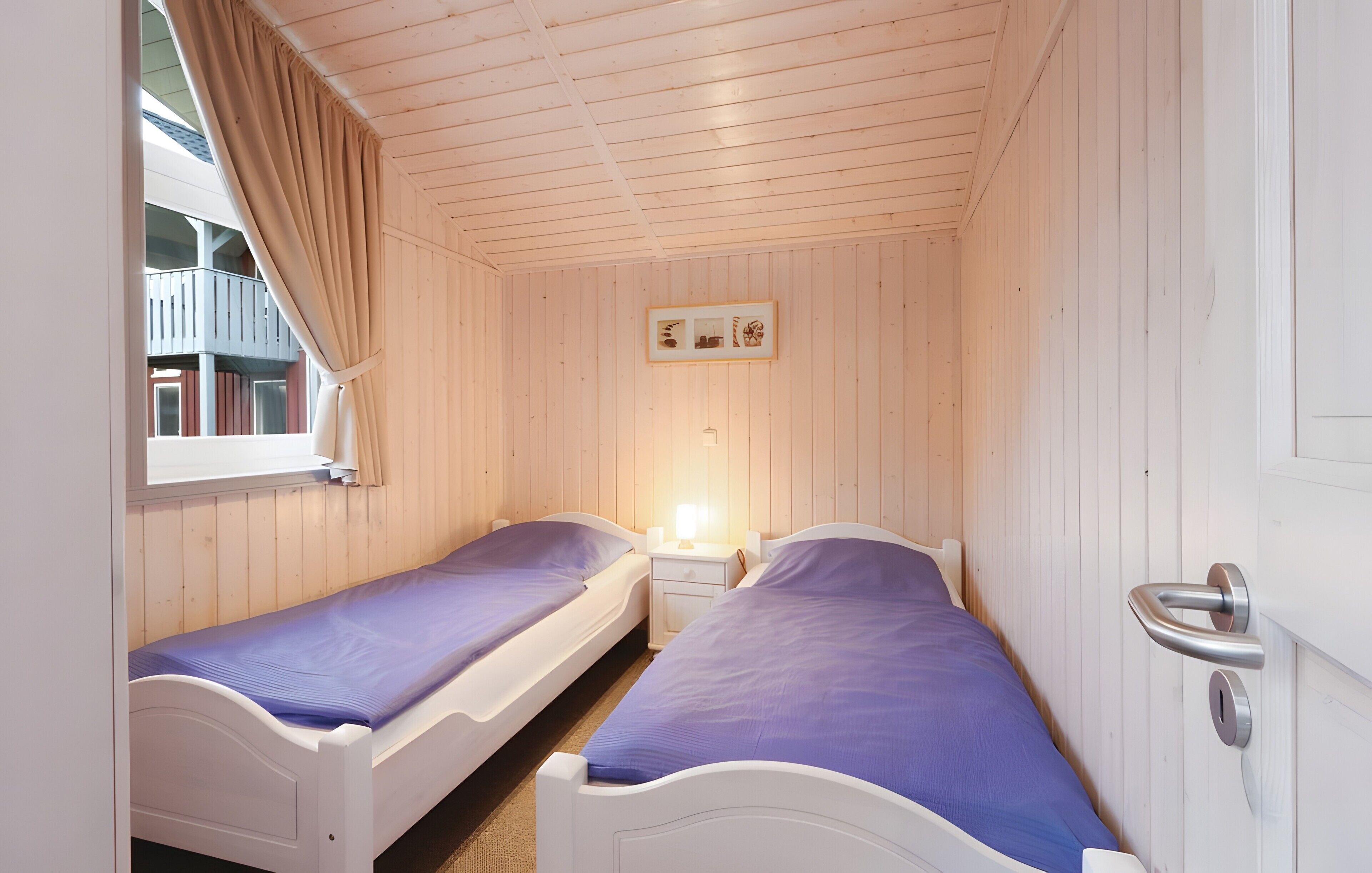 Una habitación con dos camas individuales, una ventana con cortinas, una mesita de noche con lámpara y una puerta con pomo.