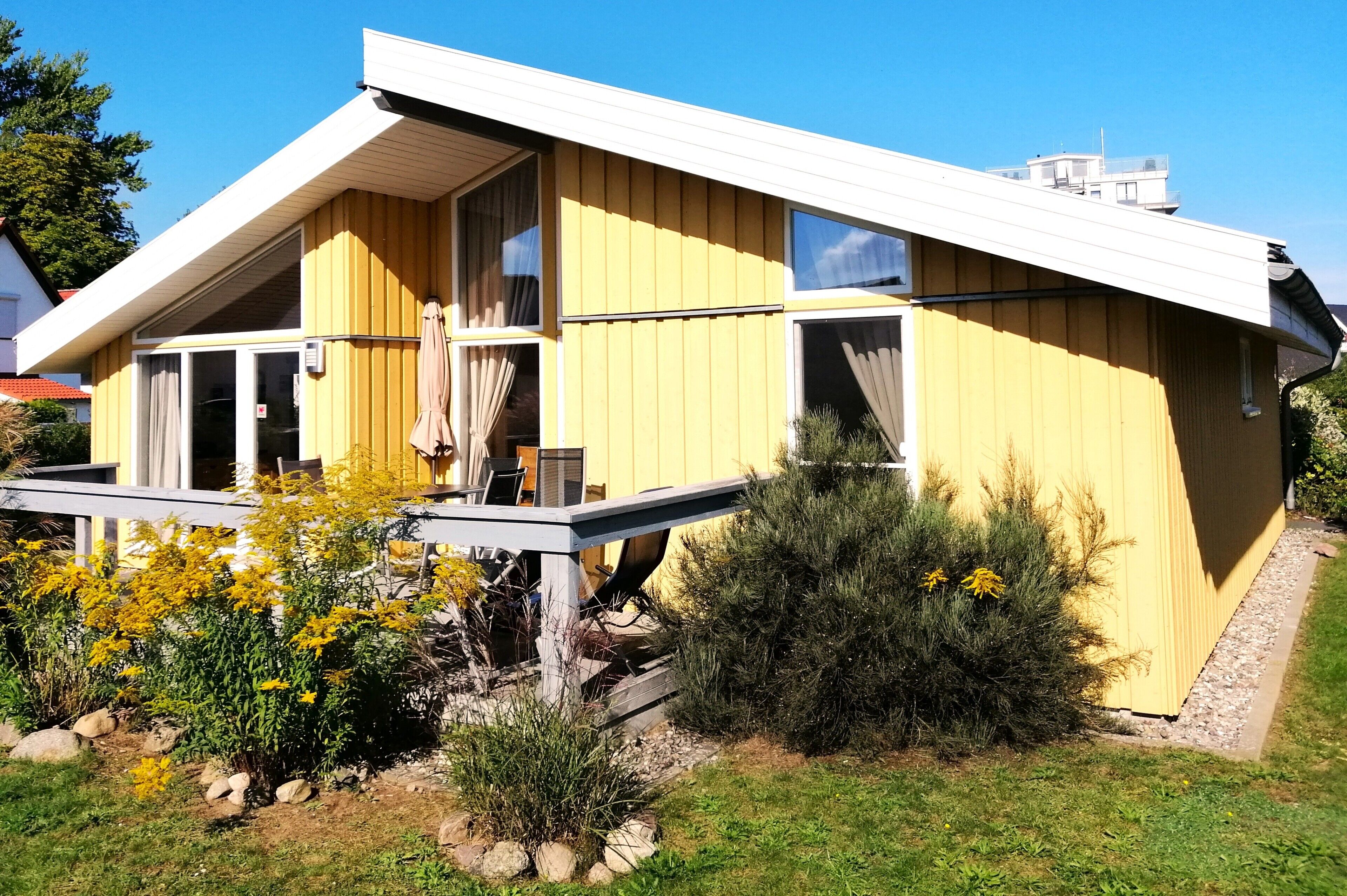 Ein gelbes Haus mit Satteldach, einer Terrasse und einem Fenster.