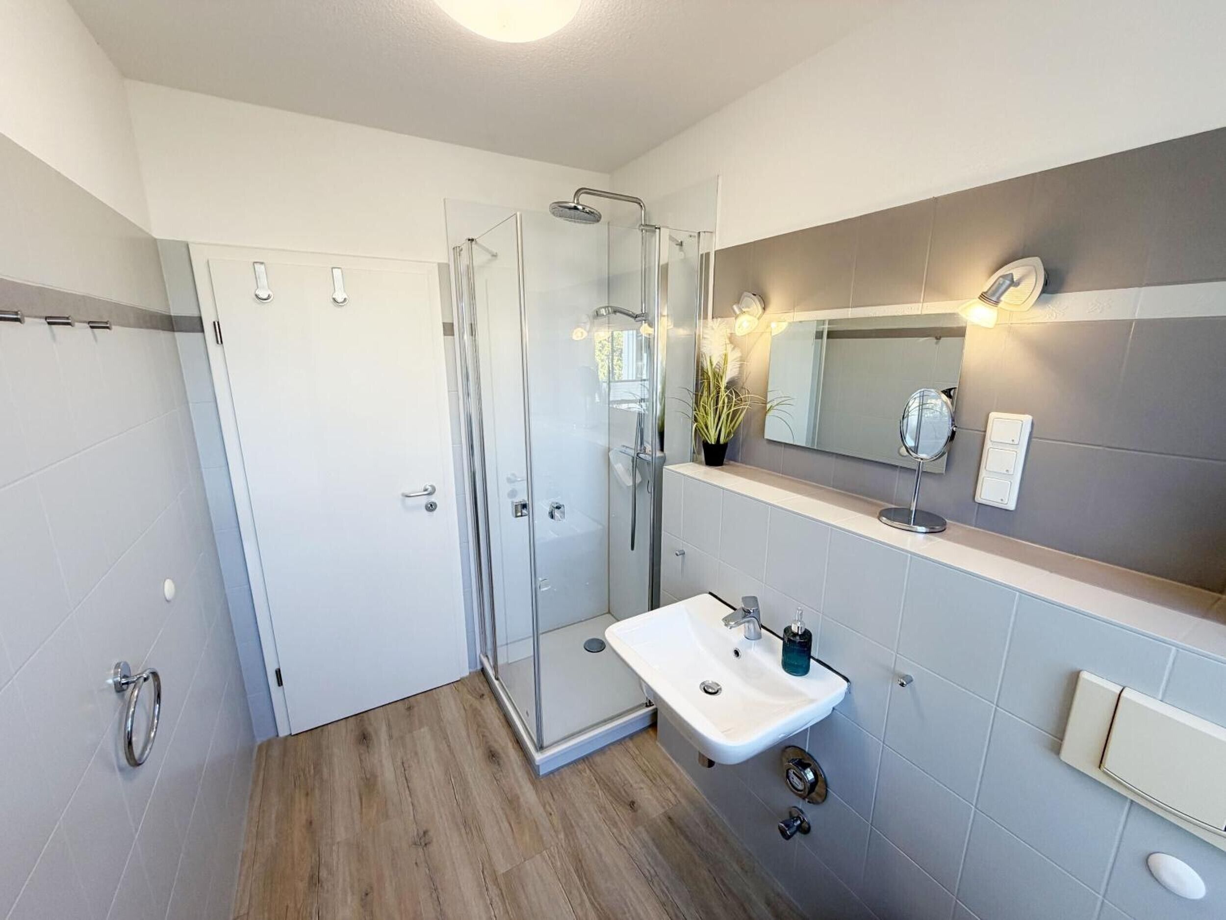 Ein modernes Badezimmer mit einer Duschkabine aus Glas, einem weißen Waschbecken und einem Spiegel darüber.