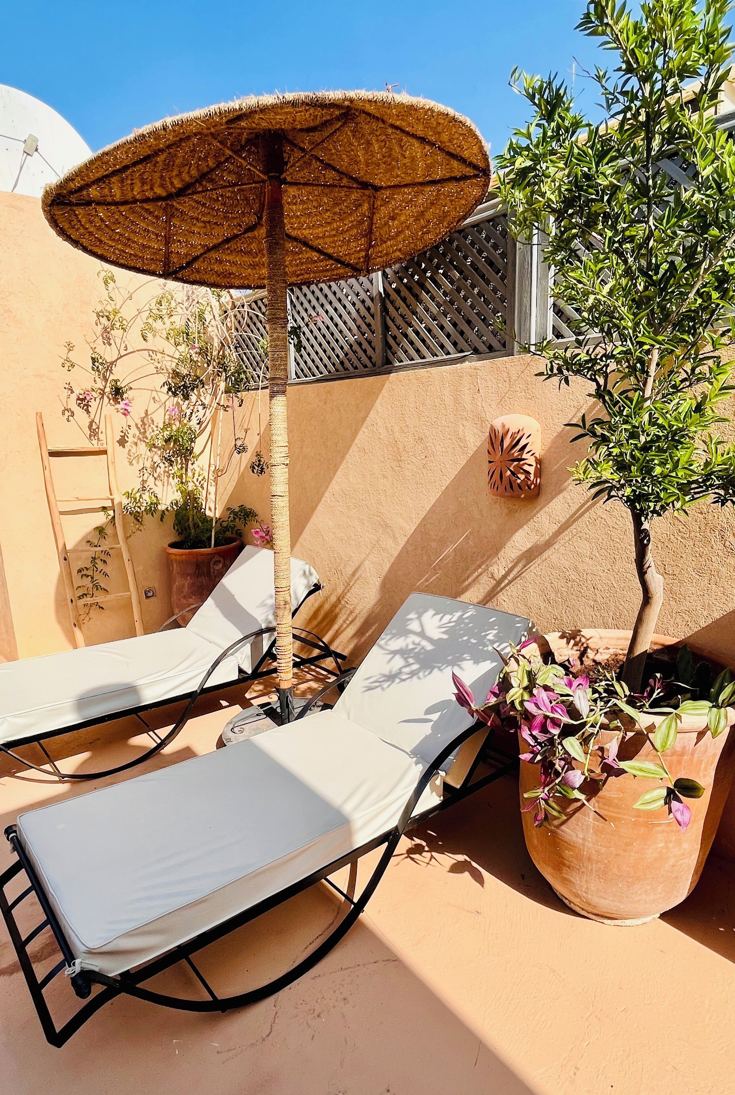 A sunlit outdoor seating area with two lounge chairs and a woven umbrella.