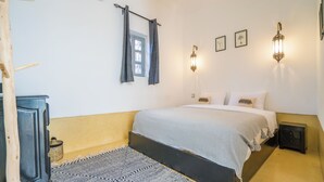 Ein Schlafzimmer mit einem Bett, Nachttischen, einem Fenster mit Vorhängen, Wandleuchten und einem Teppich.