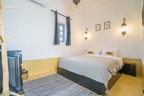 Ein Schlafzimmer mit einem Bett, Nachttischen, einem Fenster mit Vorhängen, Wandleuchten und einem Teppich.