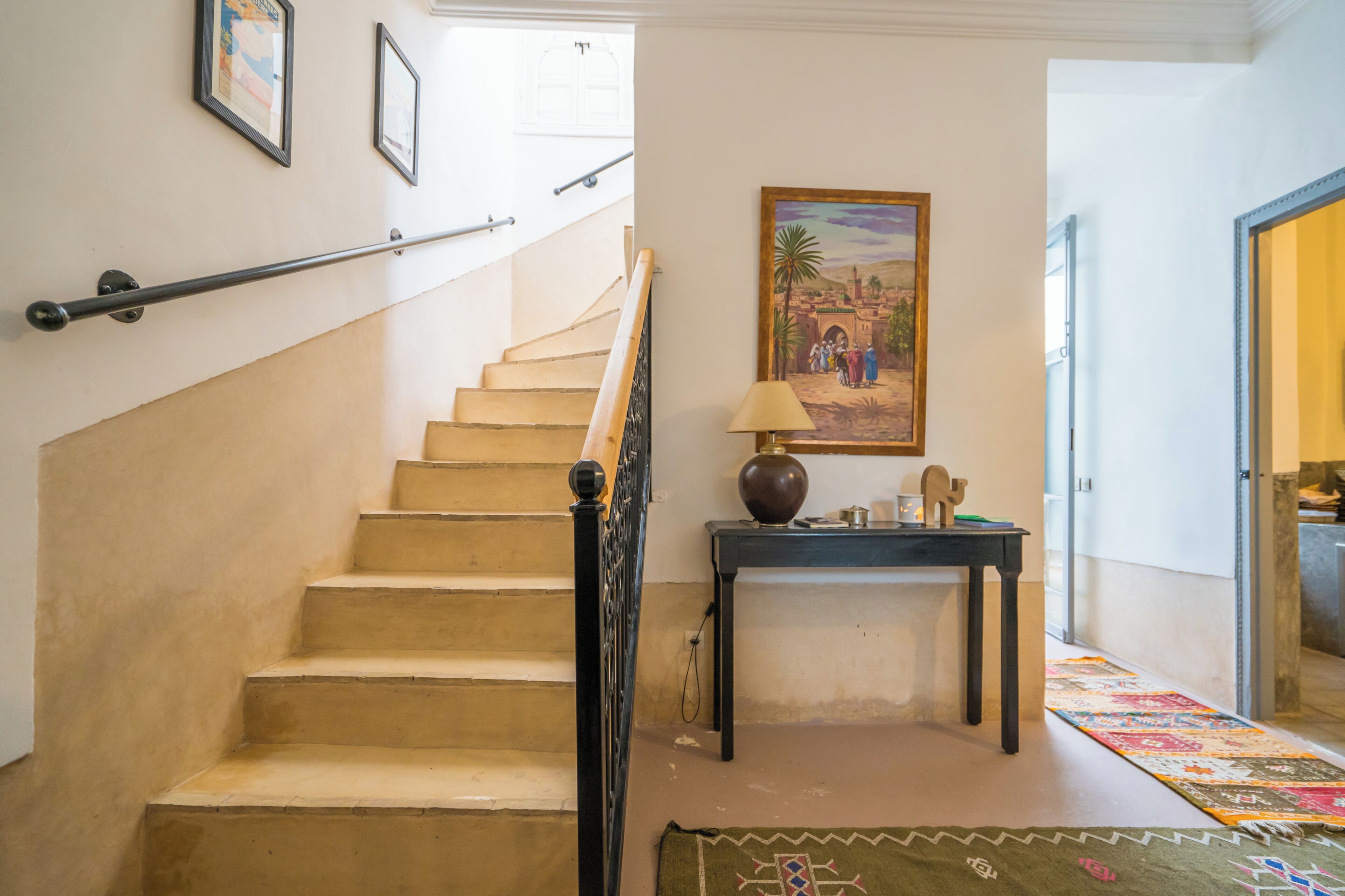 A staircase with a handrail, a painting on the wall, and a table with a lamp and decorative items.
