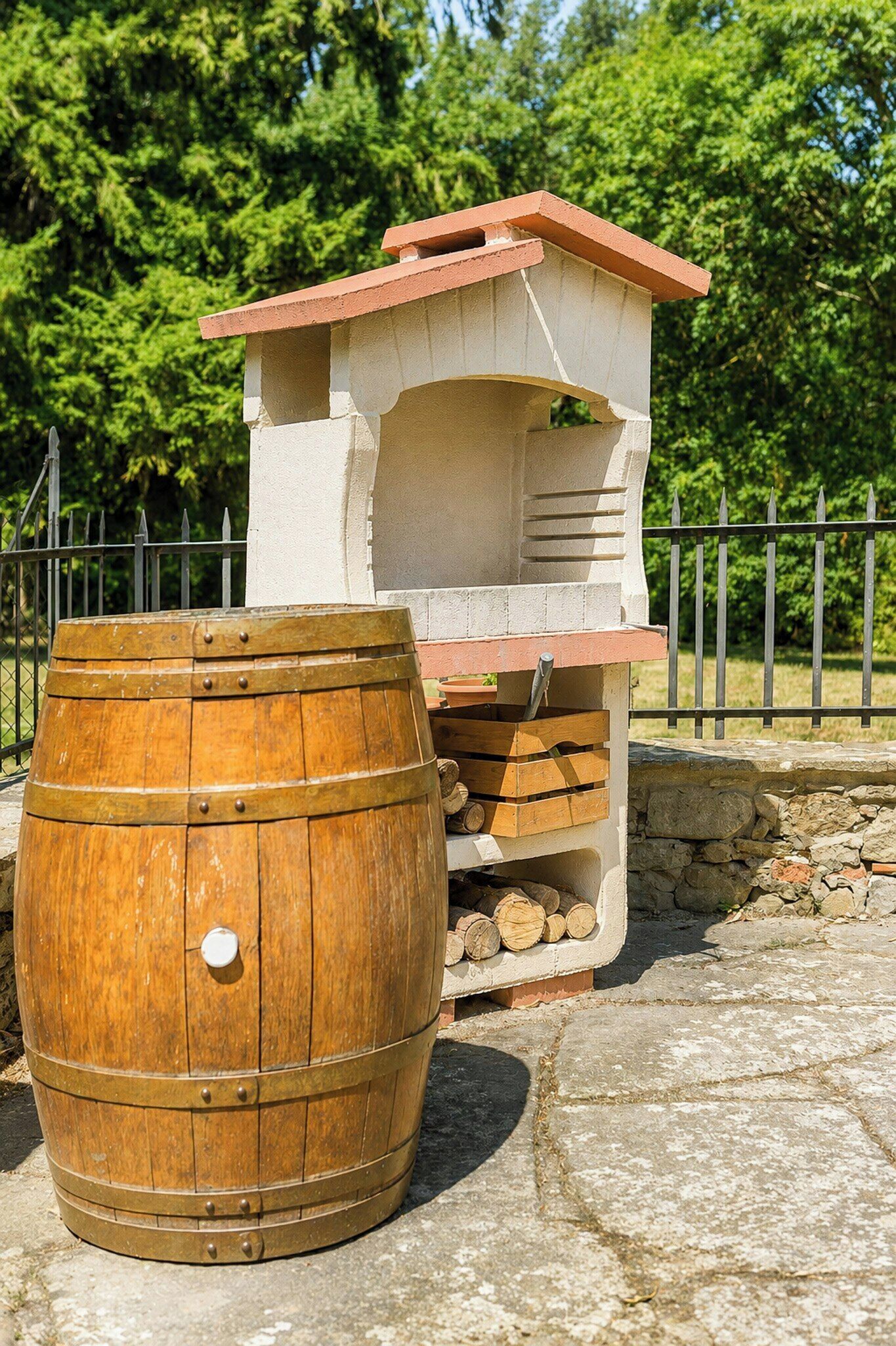 A rustic outdoor structure with a brick chimney, a wooden barrel, and a metal fence in the background.
