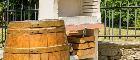 A rustic outdoor structure with a brick chimney, a wooden barrel, and a metal fence in the background.