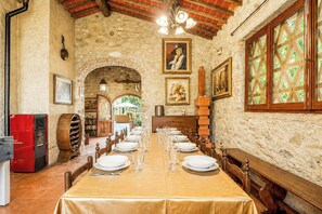 A dining area with a long table set for a meal, stone walls, wooden beams, and a view through a window. - Independent villa among Chianti vineyards (Greve in Chianti)