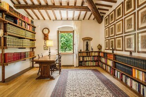 A library with wooden bookshelves, a wooden table, and a patterned rug. - Independent villa among Chianti vineyards (Greve in Chianti)