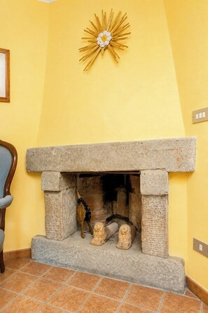 A stone fireplace with a decorative sunburst above it, set in a room with yellow walls and a tiled floor. - Independent villa among Chianti vineyards (Greve in Chianti)