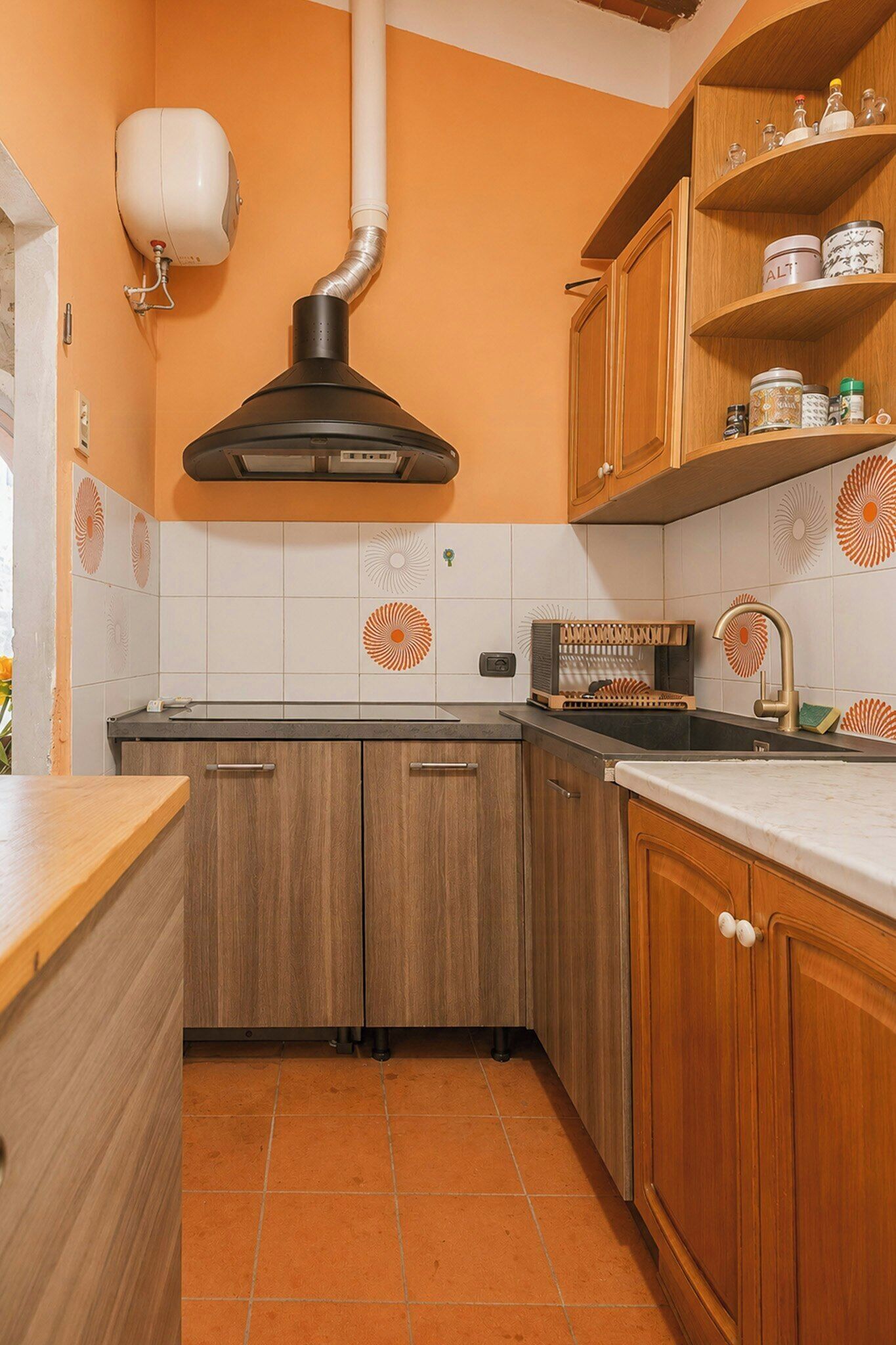 Una cucina con mobili in legno, una cappa aspirante nera e uno schienale piastrellato.