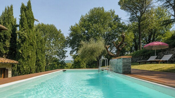 A swimming pool with a wooden deck, a waterfall feature, and lounge chairs with umbrellas. - Independent villa among Chianti vineyards (Greve in Chianti)