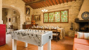 A room with a foosball table, a dining table set for four, a fireplace, and stone walls. - Independent villa among Chianti vineyards (Greve in Chianti)