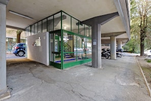 L'ingresso di un edificio con una porta in vetro, una scala e un'area di parcheggio con auto e una motocicletta.