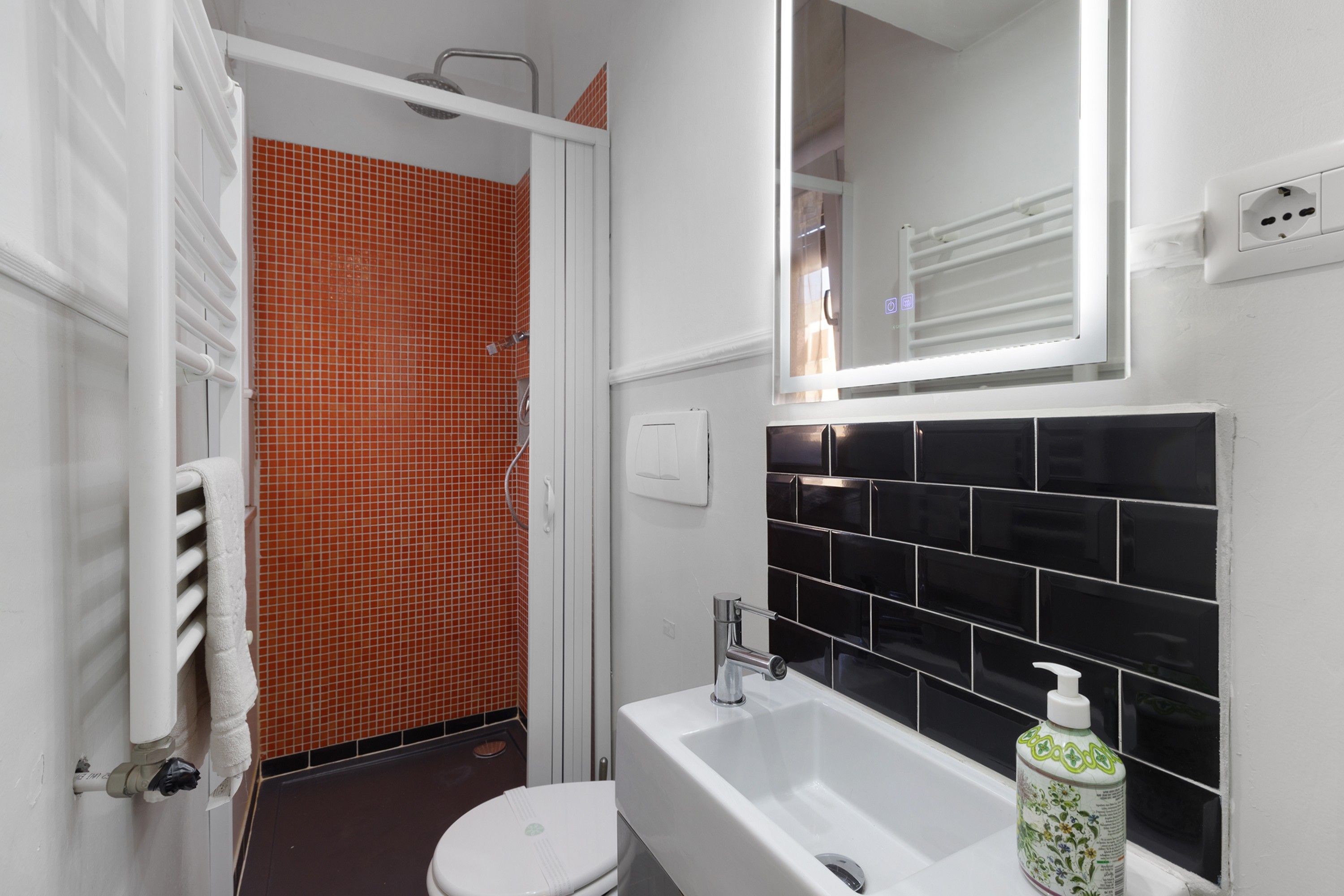 Un bagno con una vasca da bagno bianca, un WC bianco e una zona doccia con piastrelle arancioni.