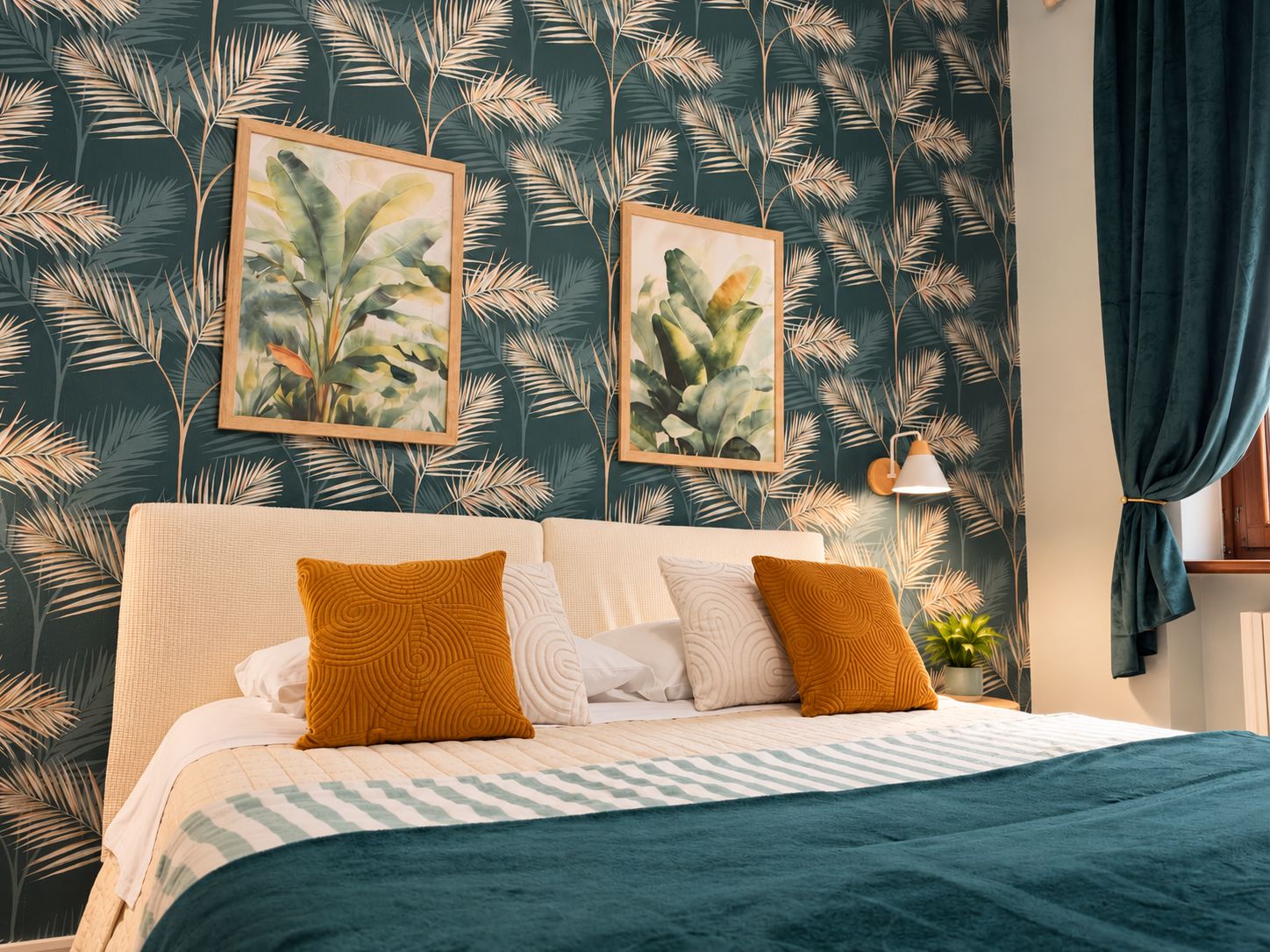 Una camera da letto con un letto, due stampe botaniche incorniciate, una lampada da comodino e una pianta in vaso.