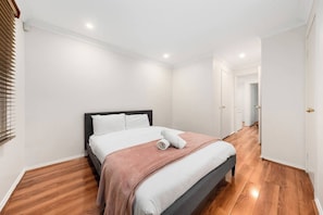 A bedroom with a bed, a wooden floor, and a white wall. - Charming Family Home | Pool & Entertainer's Deck (Carlingford)