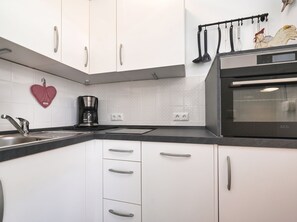 Uma cozinha moderna com armários brancos, bancada preta, cafeteira e um enfeite em formato de coração.