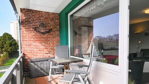 Un balcón con mesa y sillas, un muro de ladrillo y vistas al exterior.