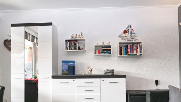 Una cocina moderna con armarios blancos, un área de comedor con un sofá de cuero negro, y una estantería con libros y objetos decorativos.