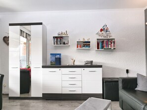 A modern kitchen with white cabinetry, a dining area with a black leather couch, and a bookshelf with books and decorative items. - Ankertied: Your cozy vacation apartment in Büsum, near the sea (Büsum)