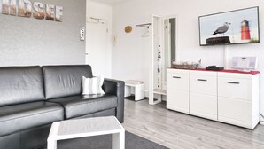 Una sala de estar moderna con un sofá de cuero negro, una mesa de centro blanca y un mueble blanco con encimera roja.