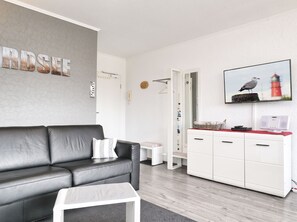 A modern living room with a black leather sofa, a white coffee table, and a white cabinet with a red countertop. - Ankertied: Your cozy vacation apartment in Büsum, near the sea (Büsum)