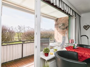 A balcony with a view of trees and a brick wall, a small table with a red tablecloth, and a chair. - Ankertied: Your cozy vacation apartment in Büsum, near the sea (Büsum)