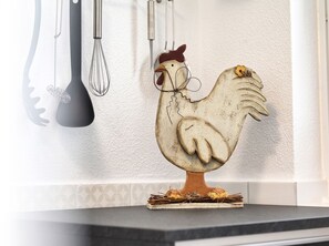 A rustic kitchen with a decorative rooster on a shelf, a whisk, and a ladle hanging on the wall. - Ankertied: Your cozy vacation apartment in Büsum, near the sea (Büsum)