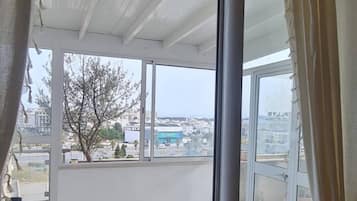 Habitació amb un gran finestral corredís que dona a una zona exterior amb terra de rajola i vista a la ciutat.
