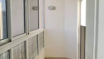 A narrow corridor with tiled flooring, large windows on one side, and a door on the other.