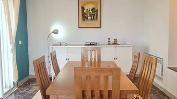 Un comedor con una mesa rectangular y seis sillas, una cocina al fondo y un cuadro en la pared.